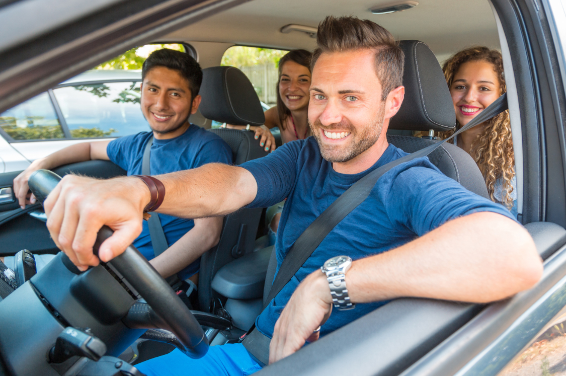 A group of people in the car looking a the camera through the drivers window.