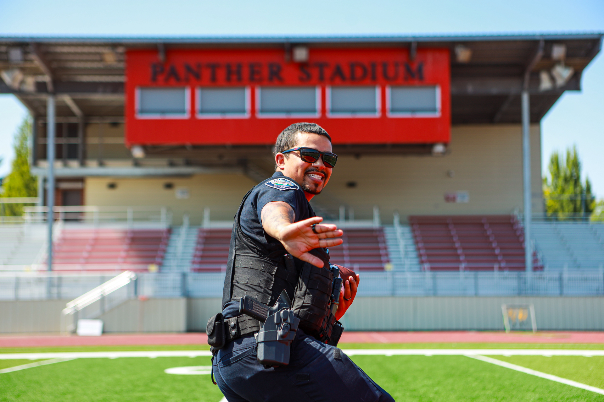 officer preston putting his hand out in a defensive position and smiling on a football field, with the stadium behind him.