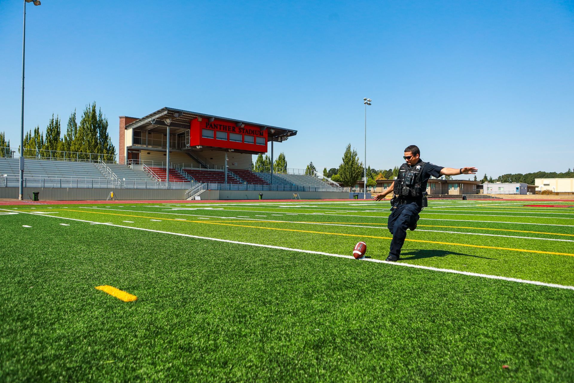 officer preston getting ready to kick a ball on a football field, with the stadium in the background