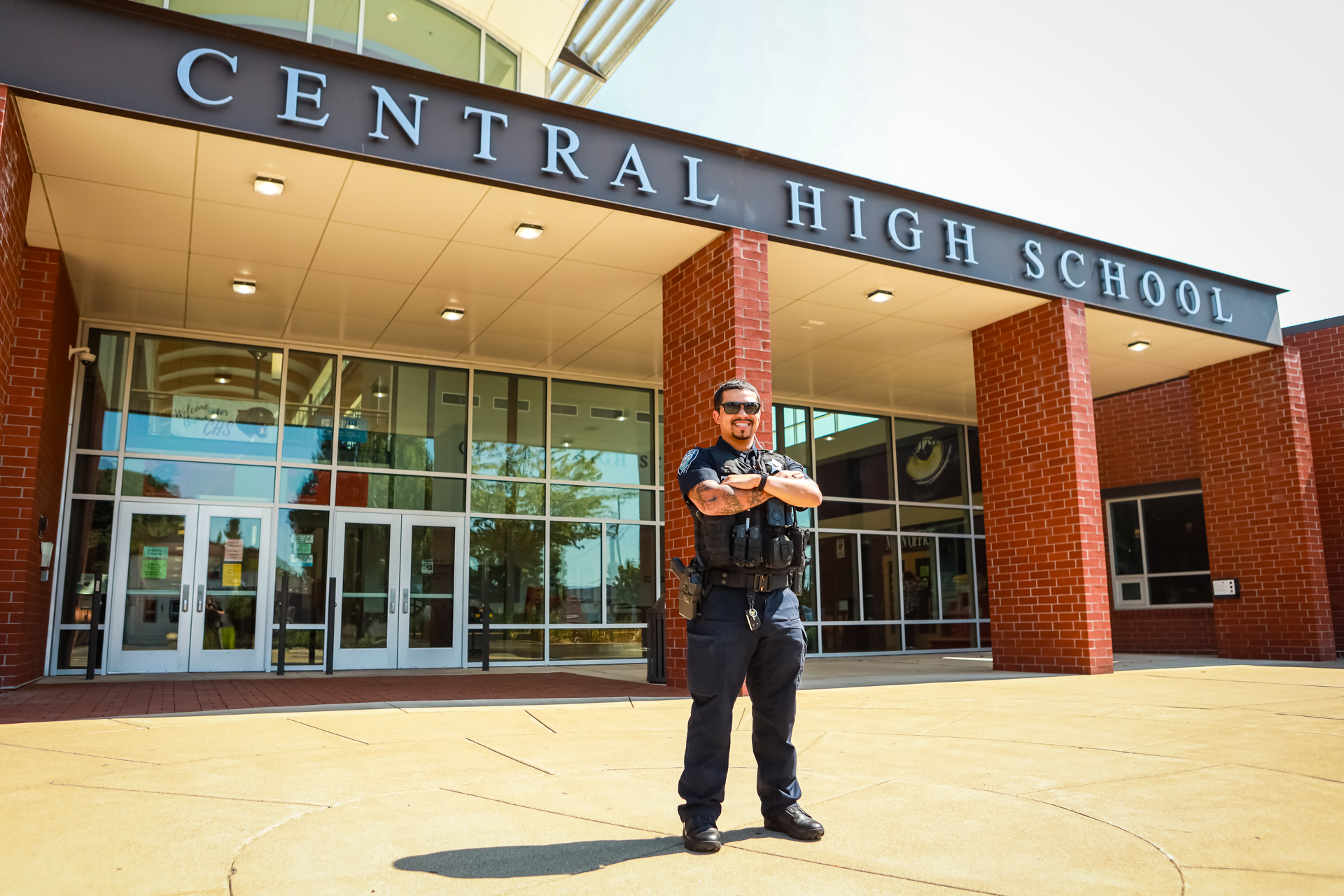 officer preson smiling in front of the front doors of central high school. His arms are crossing but welcoming