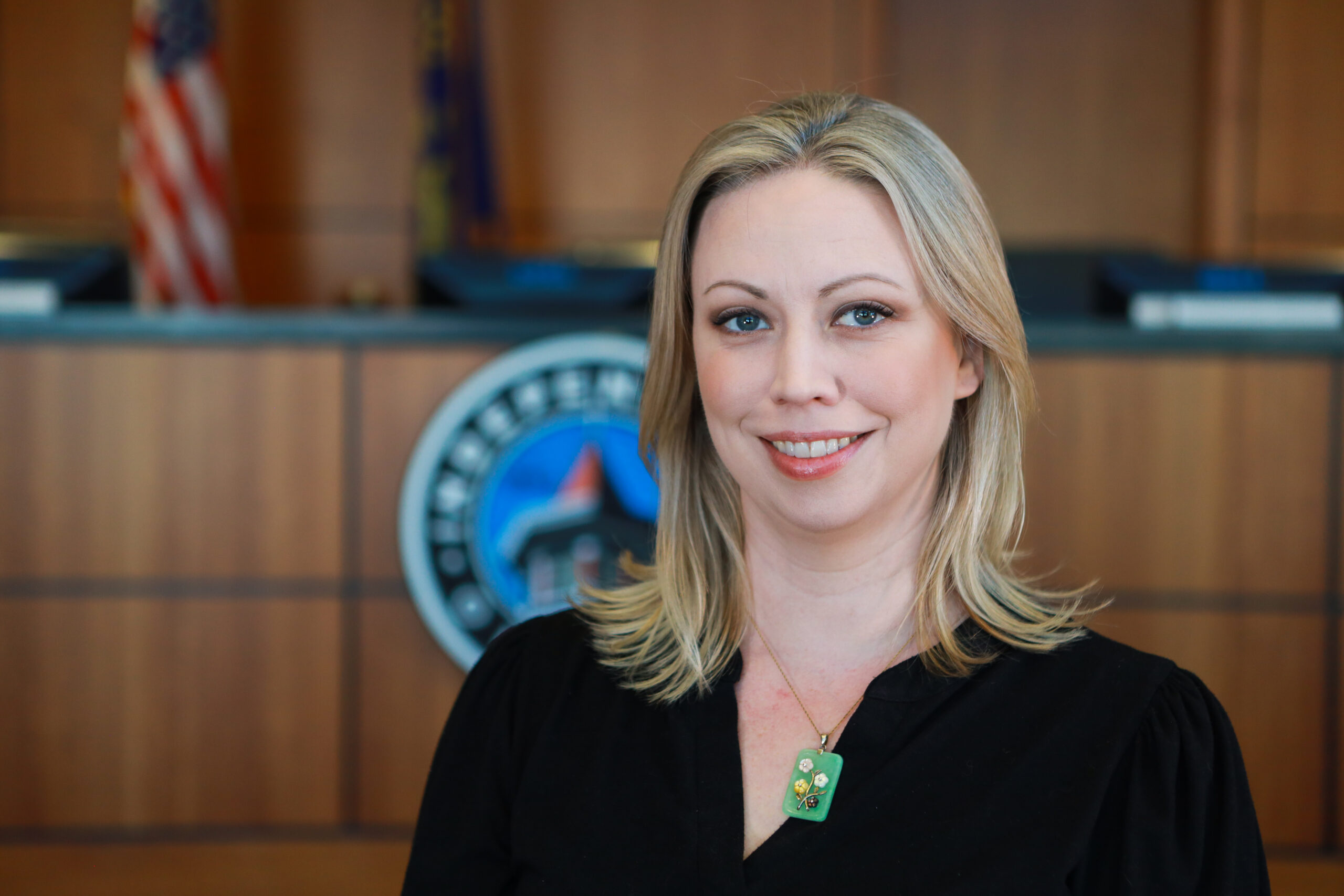 a medium headshot of Finance Director Amanda Carey. She is located in the city council chambers, with the dais, city logo, and American flag in the background.