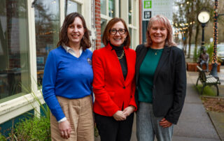 three women stand and smile in a line. cityscape is in the background