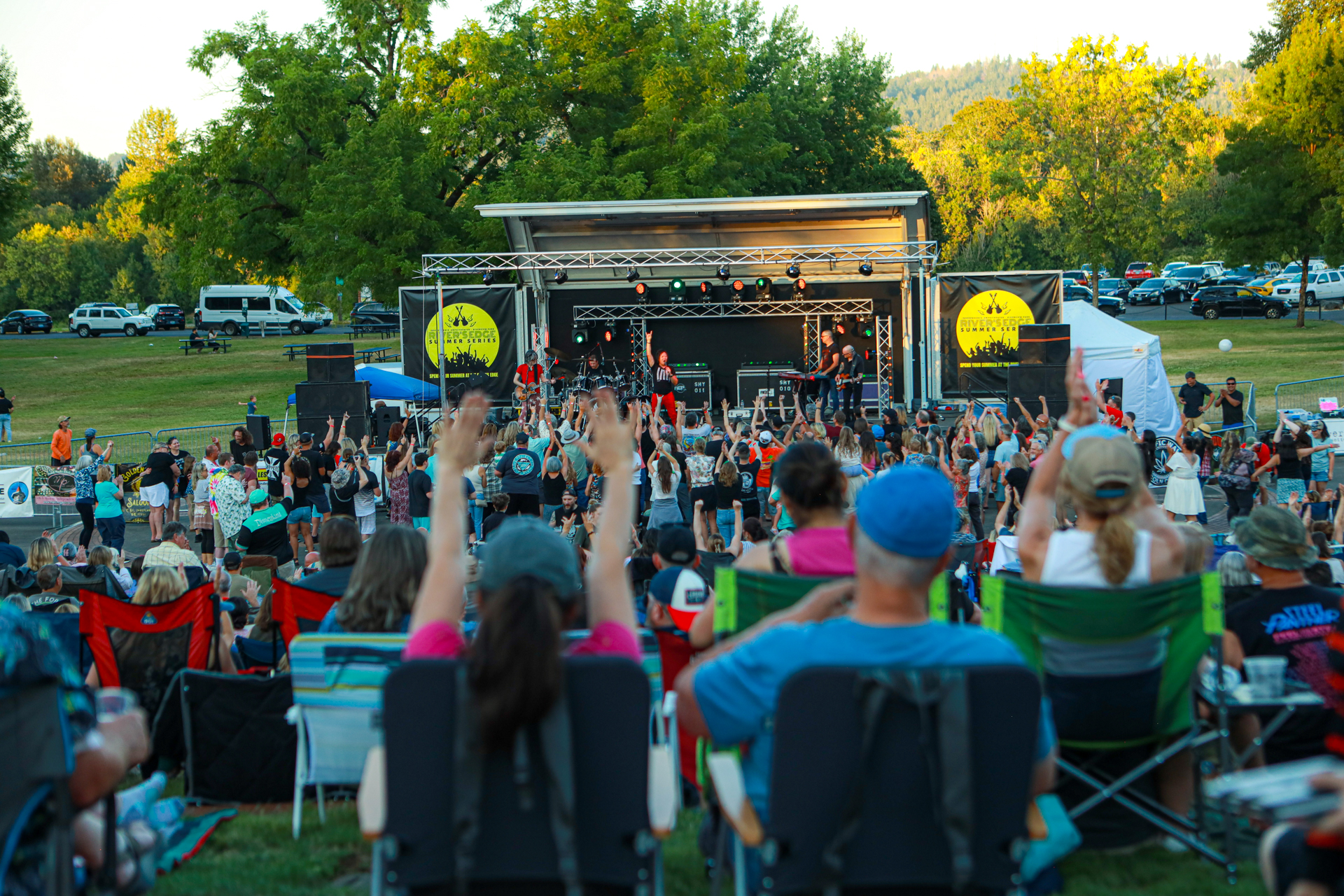 Attendees at an outdoor concert, standing and swaying to the music, surrounded by vibrant stage lights and decorations.