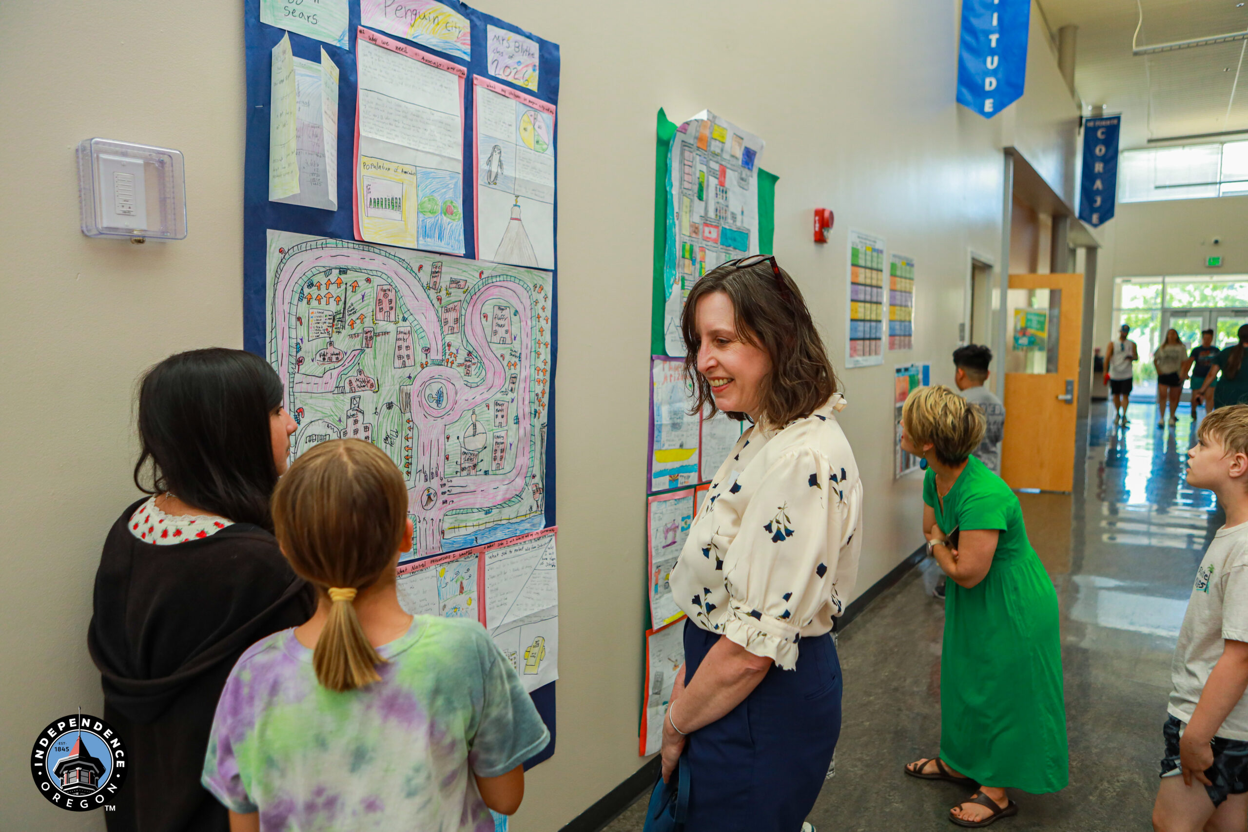 Visitors admire colorful student artwork displayed on walls during an educational event in a school hallway.