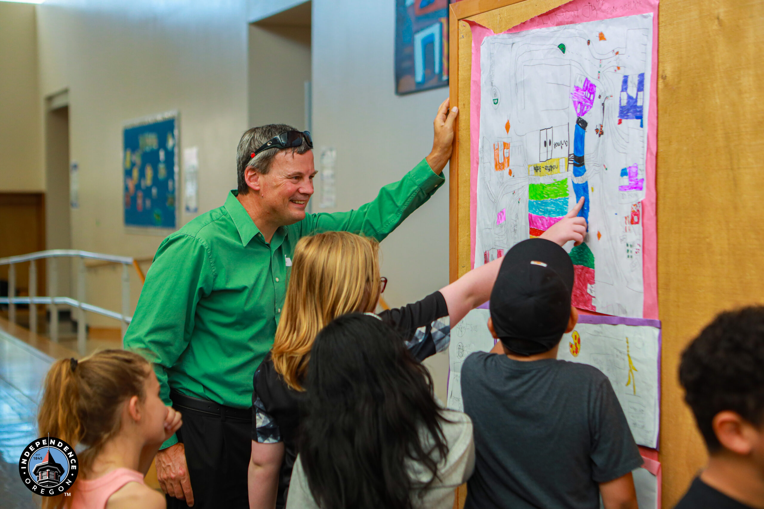 A child and an adult discussing colorful artwork on a wall, showcasing creative projects and maps in a classroom setting.