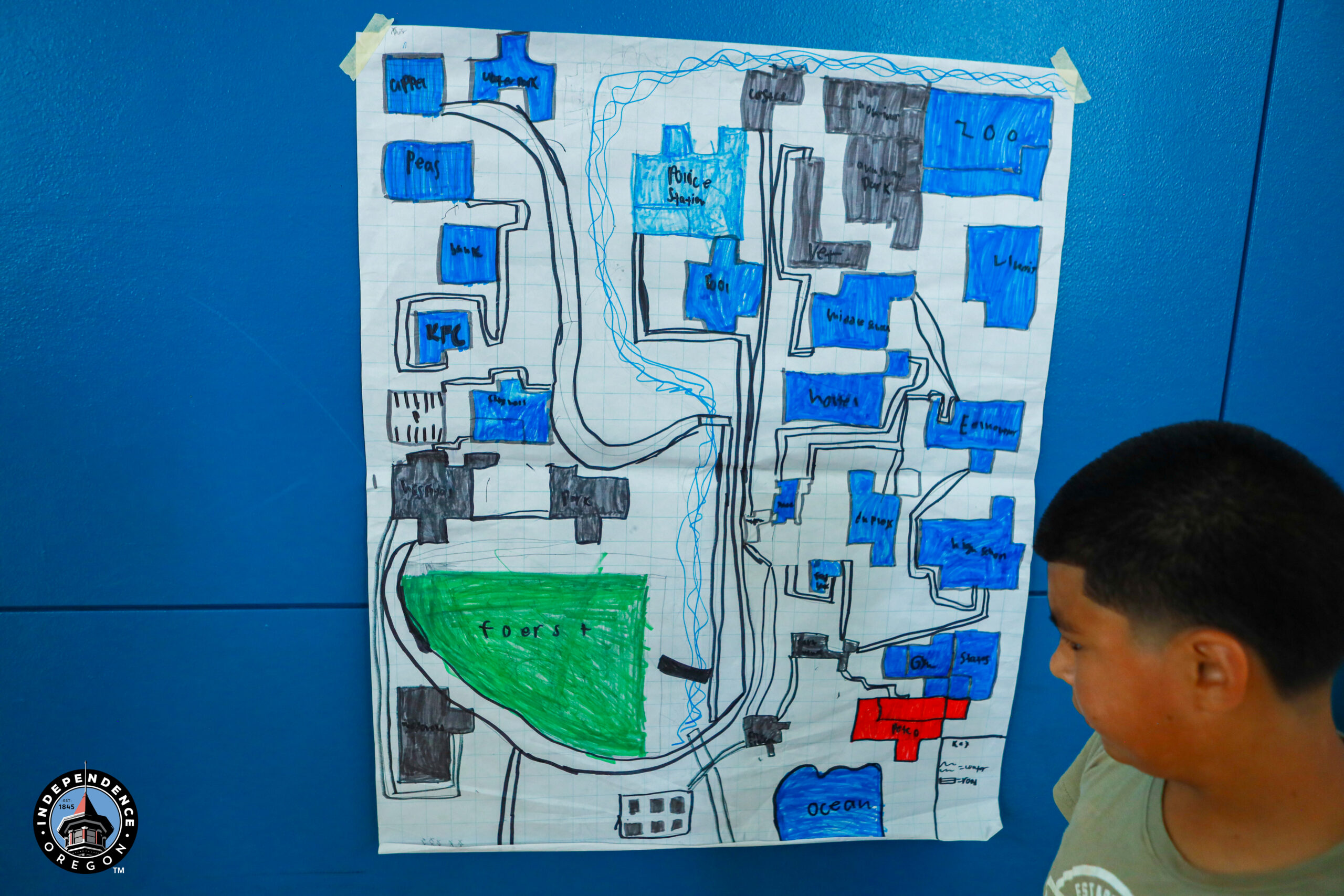 A colorful hand-drawn map featuring various locations, with a boy observing it, set against a blue background.