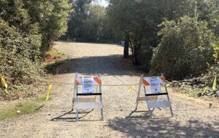 two sandwich board signs and a chain prevent entrance to a gravel lot.
