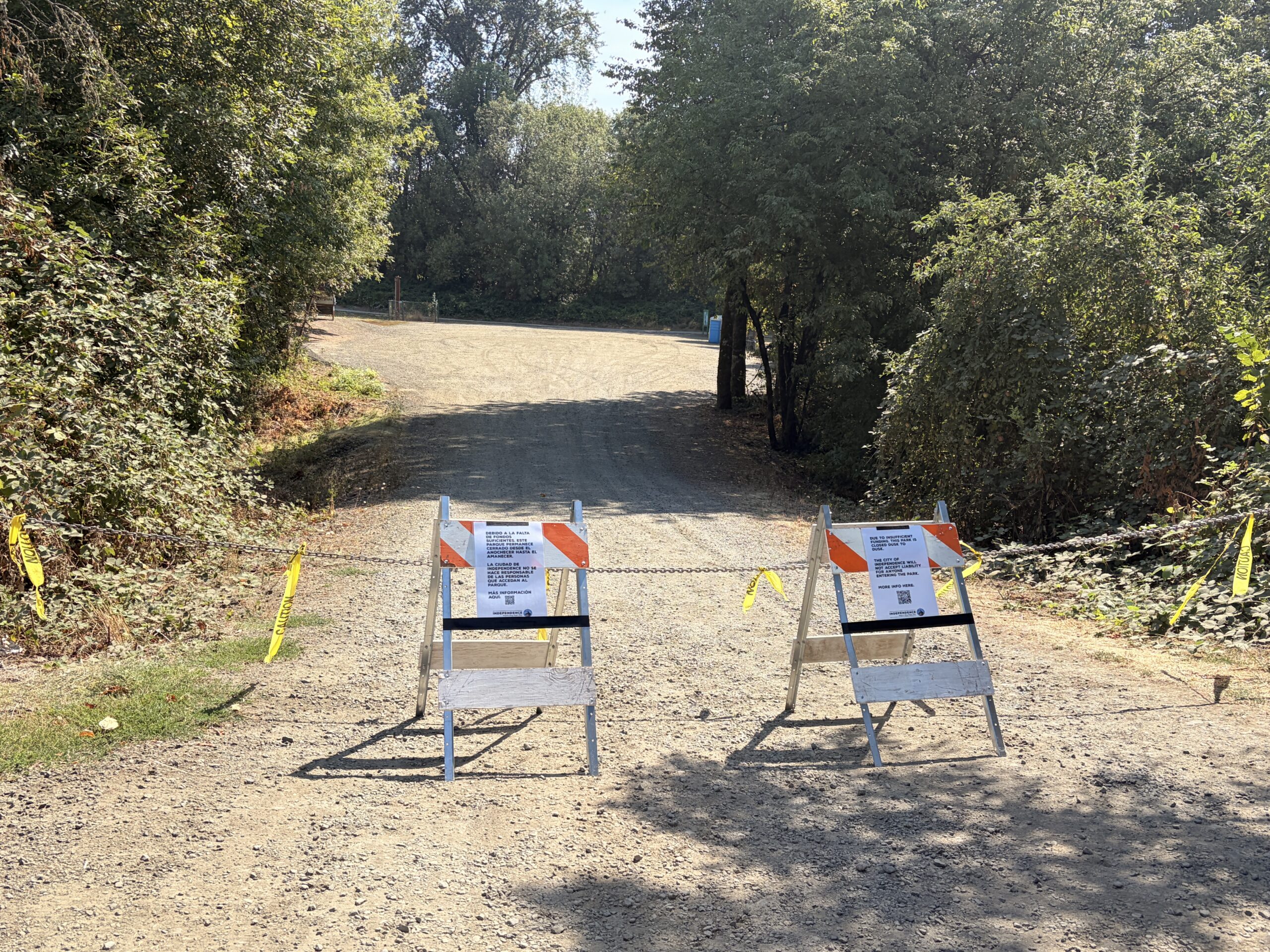 two sandwich board signs and a chain prevent entrance to a gravel lot.
